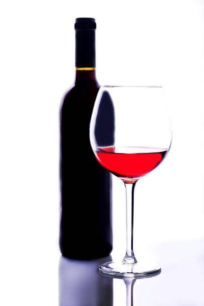 A thin-stemmed glass of red wine and a bottle of wine. A glass of red wine on a white background. Reflection. - Photo, Image