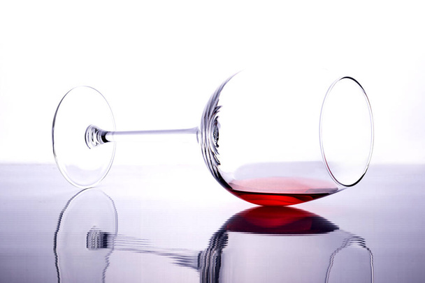 The glass of red wine is on its side. A glass of red wine on a white background. Reflection. - Fotografie, Obrázek