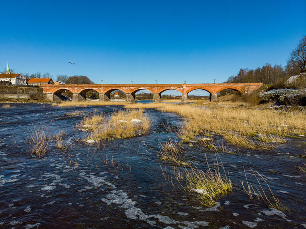 Hermosa vista soleada del río wenta que fluye hacia el viejo puente de ladrillo en la antigua ciudad rural histórica de Kuldiga. Foto tomada en cálido Primavera de Europa
. - Foto, imagen