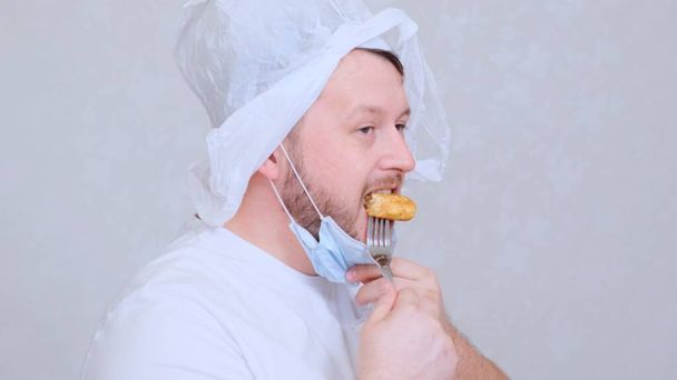bearded man in a mask and a bag on his head eats a cutlet. Fear of infection. Psychological assistance in case of panic. Joke situation. - Photo, Image