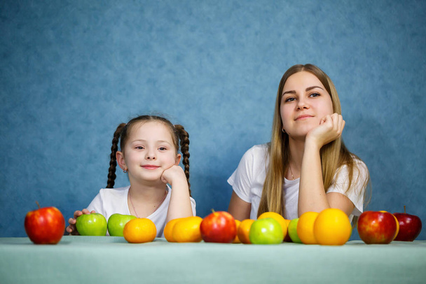 Маленька дівчинка і мама граються з фруктами і дурнем. Вони носять футболки.
 - Фото, зображення