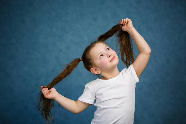 маленькая девочка в белой футболке и джинсах развлекается со своими волосами
 - Фото, изображение