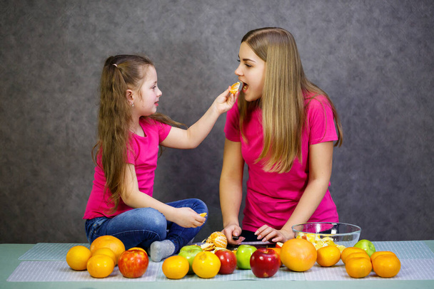 Tochter und Mutter schneiden einen Obstsalat aus Apfel-Orange und Mandarine - Foto, Bild