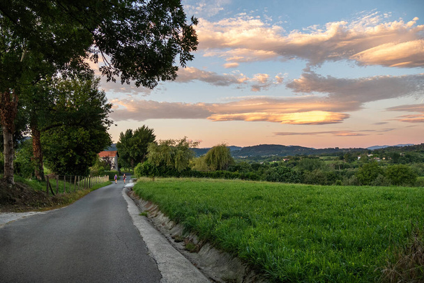 Estrada com viajantes no campo. Nuvens coloridas incríveis sobre o campo. Irun, País Basco, Espanha
. - Foto, Imagem