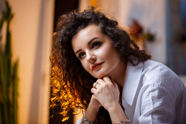 Beautiful young girl model with curls posing. She is wearing a white shirt and jeans. - Fotó, kép