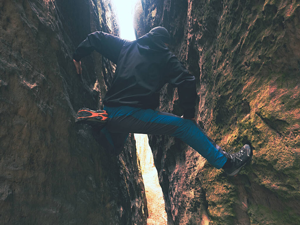 Funny man is climbing in thin distance between two rocks. Dark corner below rocky wall. - Foto, imagen