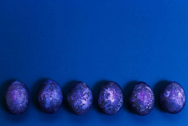 Easter card. Eggs with marble stone blue effect painted with natural dye carcade flower on blue sparkling background with blank space for text. Top view. Flat lay - Fotografie, Obrázek