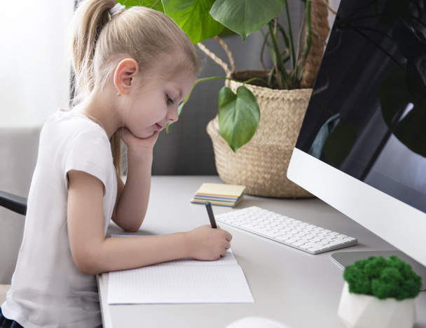 Stay at home for the quarantine prevention of the coronavirus pandemic. Little girl with blond hair sits at a table and does homework.  - Photo, Image