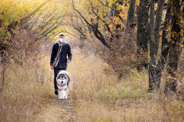 A man in a medical mask walks a dog in a forest during quarantine - Fotó, kép