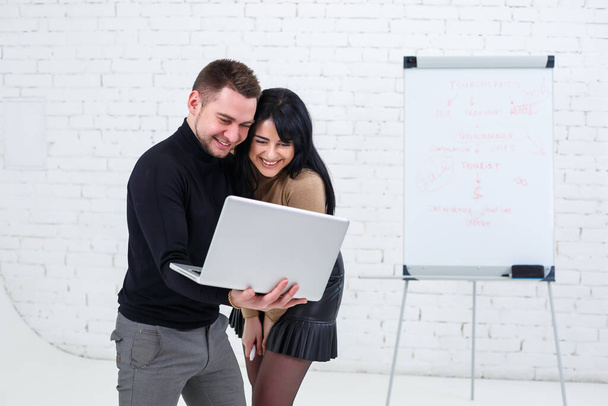 Empresário sorridente e gerente mulher estão de pé com laptop e olhando para a tela. Fique em um fundo branco
. - Foto, Imagem