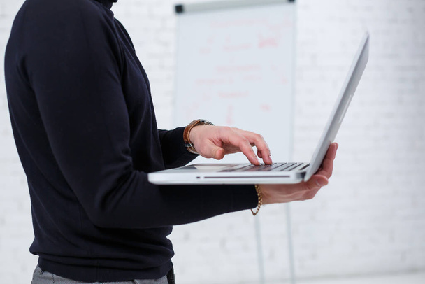 Een mannelijke zakenman manager glimlacht en staat met een laptop in zijn handen en kijkt naar het scherm. Staat op een witte achtergrond. - Foto, afbeelding