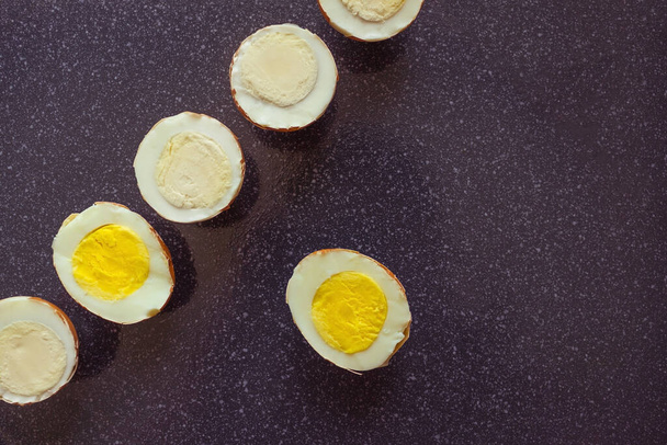 Boiled eggs are cut across. One, cut along, is looking for its half. Another, different among many, is special. A dark background, top view. - Photo, Image