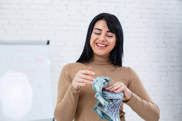 Foto de uma mulher encantadora com um sorriso segurando um fã de dinheiro em suas mãos
 - Foto, Imagem