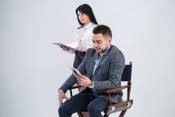 Un homme en costume est assis sur une chaise noire avec une tablette et une femme jette des documents. Les futurs hommes d'affaires sont nerveux et parlent d'un nouveau projet. Partenaires commerciaux sur fond blanc
. - Photo, image