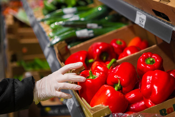 hand in a white glove takes red pepper in a store. epidemic safety - Foto, Imagen