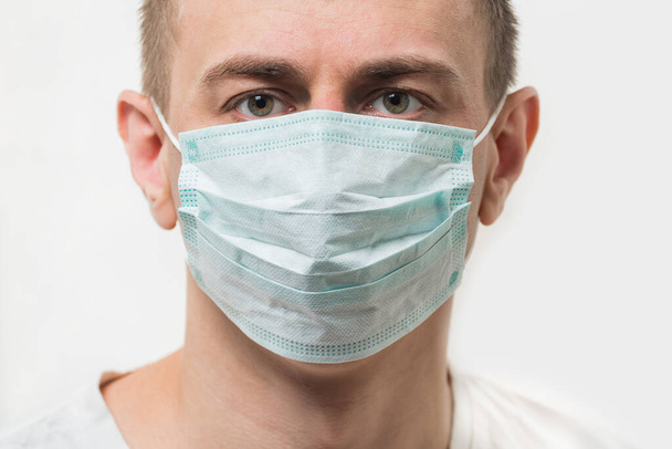 Egy eldobható maszkos férfi portréja. Orvos sztiril sebészeti maszkban. Közelről. - Fotó, kép