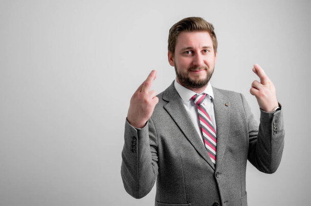 Portrait of business man wearing business clothes showing double fingers crossed isolated on grey background with copy space advertising area - Photo, Image