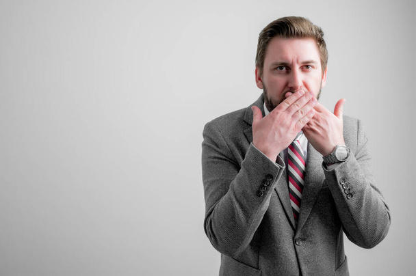 Portrait of business man wearing business clothes covering mouth like mute gesture isolated on grey background with copy space advertising area - Photo, Image