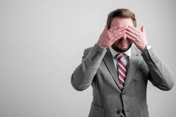 Πορτρέτο του επιχειρηματία φορώντας ρούχα επιχειρήσεων που καλύπτουν τα μάτια σαν τυφλή χειρονομία απομονώνονται σε γκρι φόντο με αντίγραφο χώρο διαφήμισης - Φωτογραφία, εικόνα
