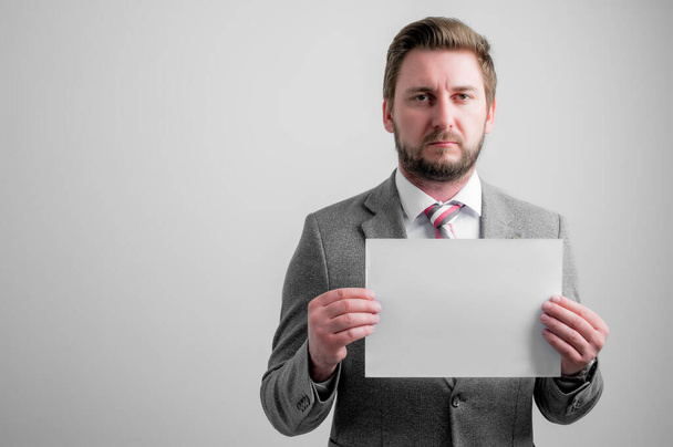 Porträt eines Geschäftsmannes in Businesskleidung, der weißes Papier auf grauem Hintergrund mit Kopierraum-Werbefläche hält - Foto, Bild