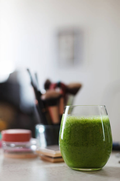 Läpinäkyvä lasi täynnä vihreä smoothie meikkipöytä. Käsitys kauniista ja terveellisestä sekä sisältä että ulkoa
. - Valokuva, kuva