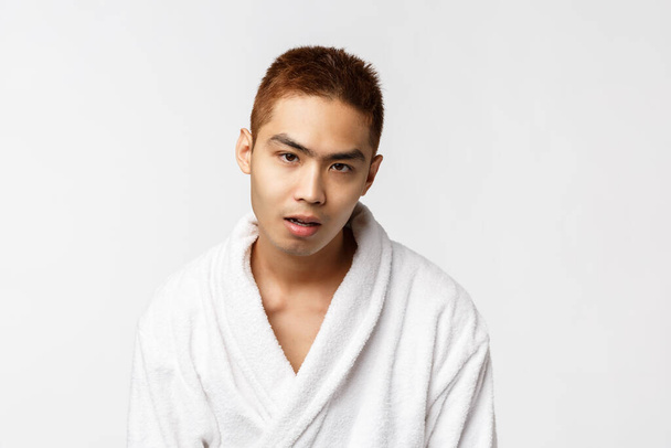 Beauty, spa and leisure concept. So lame. Portrait of reluctant and indifferent asian man in bathrobe, open mouth and say blah, feel bored and indifferent, hear boring conversation, white background - Photo, Image