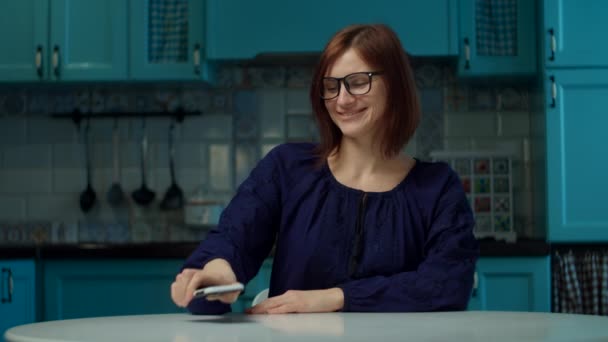 Young 30s woman in glasses making online order via mobile app on kitchen at home during coronavirus COVID-19 quarantine. Funny concept of toilet paper deficit.  - Video, Çekim