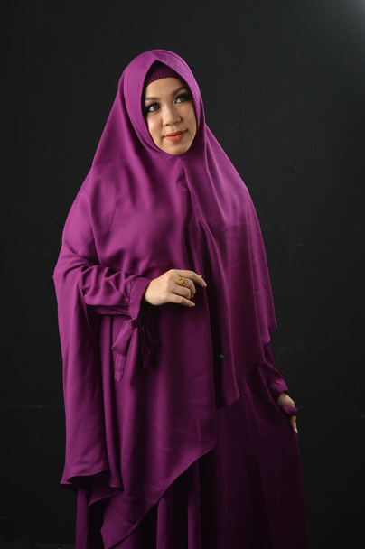 portrait of a beautiful muslim woman wearing a violet headscarf isolated on black background - Photo, Image