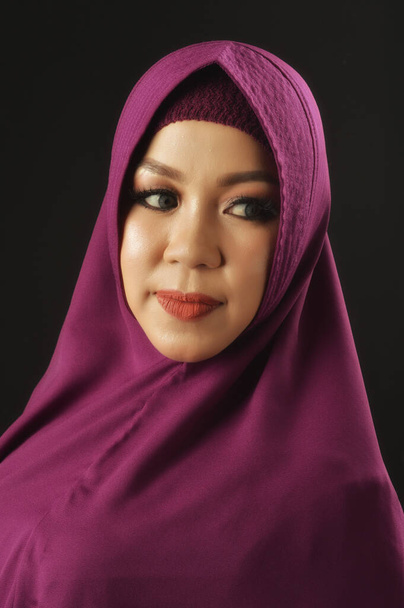 πορτρέτο μιας όμορφης μουσουλμάνας γυναίκας που φοράει βιολετί μαντίλα και είναι απομονωμένη σε μαύρο φόντο - Φωτογραφία, εικόνα
