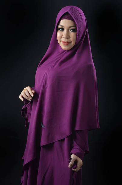 Porträt einer schönen muslimischen Frau mit violettem Kopftuch, isoliert auf schwarzem Hintergrund - Foto, Bild