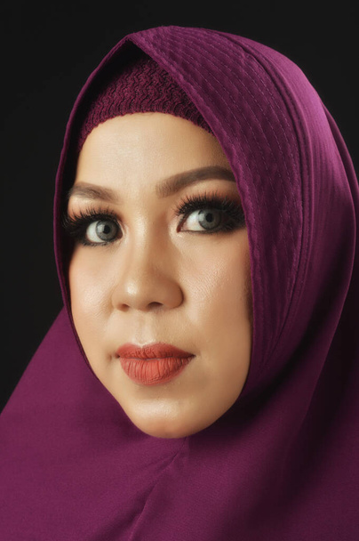 πορτρέτο μιας όμορφης μουσουλμάνας γυναίκας που φοράει βιολετί μαντίλα και είναι απομονωμένη σε μαύρο φόντο - Φωτογραφία, εικόνα