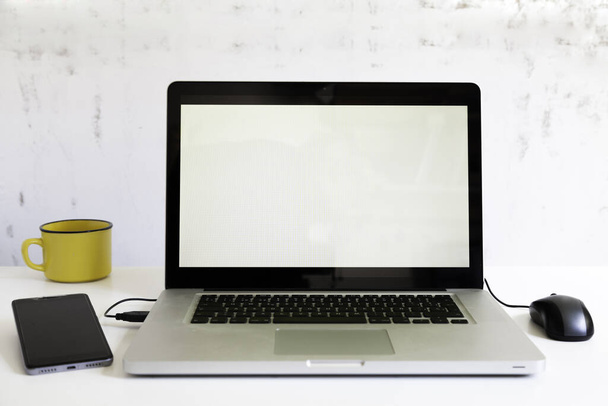 laptop met muis, smartphone en gele beker op witte tafel en rustieke witte achtergrond - Foto, afbeelding