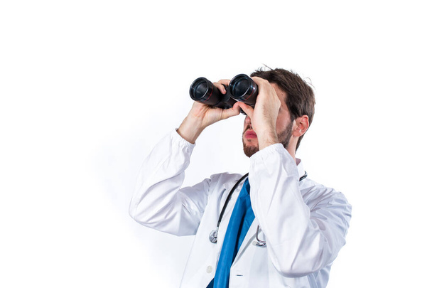 Young doctor with binoculars posing isolated on white background - Foto, afbeelding