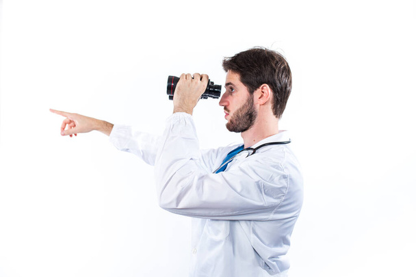 Young doctor with binoculars posing isolated on white background - Foto, Bild