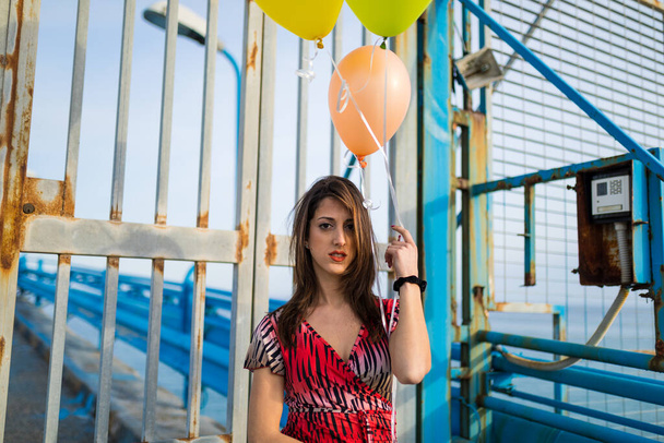 若いです女性でドレスを保持黄色の風船ポージングで桟橋によって海辺 - 写真・画像