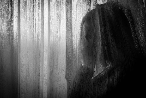 Θλιβερή γυναίκα που κοιτάζει από το παράθυρο κατά τη διάρκεια της καραντίνας λόγω ενδοοικογενειακής βίας, κοινωνικής απόστασης ή σωματικού προβλήματος - Φωτογραφία, εικόνα