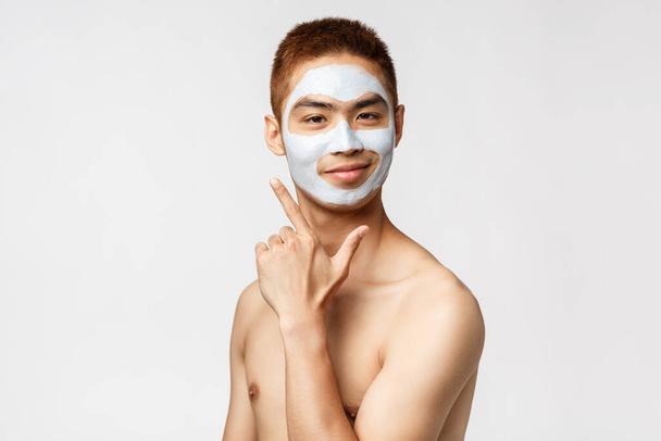 Concept beauté, soins de la peau et hygiène. Portrait de heureux, heureux jeune homme asiatique se sentant belle, vibing à la salle de bain avec crème faciale, souriant comme son apparence de visage, stand fond blanc
 - Photo, image