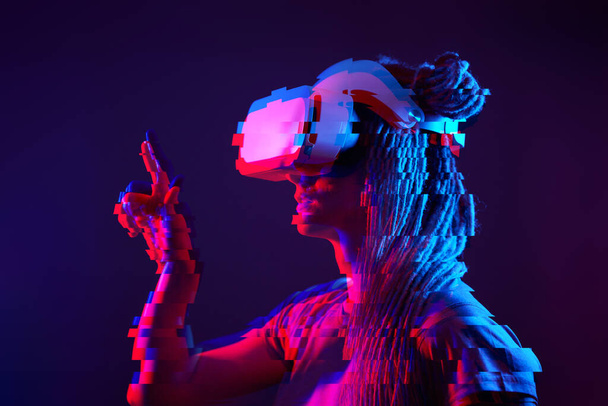Woman is using virtual reality headset. Neon light studio portrait. Image with glitch effect. - Foto, imagen