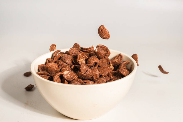 Schokolade Cornflakes fallen auf die weiße Schüssel isoliert auf weiß. Bewegung. Kopierraum. - Foto, Bild