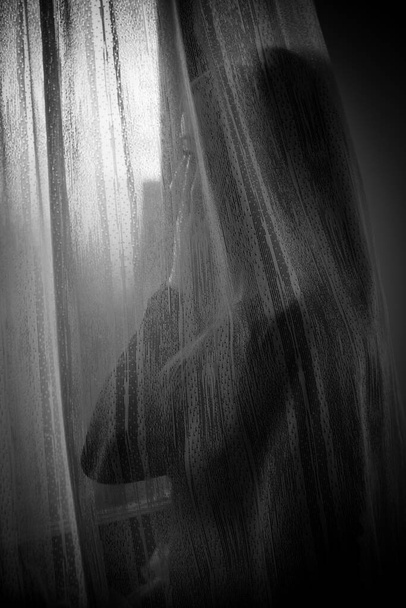 Depressieve vrouw die door het raam kijkt tijdens quarantaine als gevolg van huiselijk geweld, sociale afstand of fysieke problemen - Foto, afbeelding