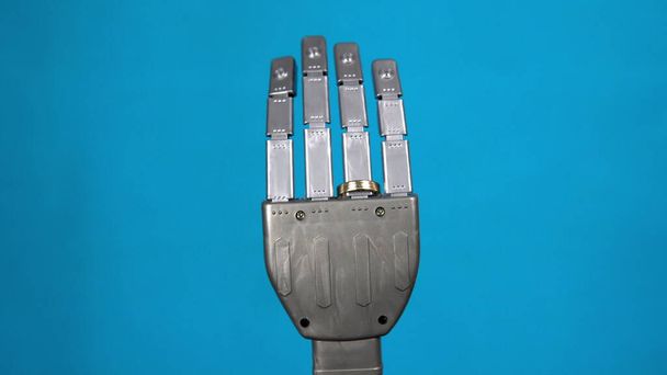 Een mechanische hand met een ring om de ringvinger. Grijze cyborg hand op een blauwe achtergrond. - Foto, afbeelding