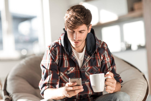 attractive young man drinking coffee and reading SMS. - Фото, зображення