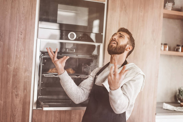 surprised man standing near the oven with burnt croissants. - Φωτογραφία, εικόνα