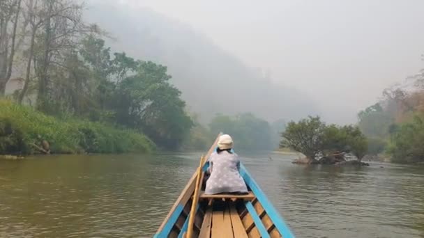 Kis fahajó navigál egy vad trópusi folyóban a zöld dzsungelben egy nővel, aki a hajó előtt ül és békésen nézi a tájat. Kék kenu a természet felfedezésére. - Felvétel, videó