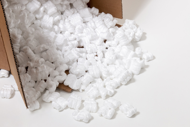Kartonnen doos morst veel polystyreen of witte piepschuim verpakkingsstukken gebruikt voor het minimaliseren van hobbels in het vervoer van goederen. - Foto, afbeelding
