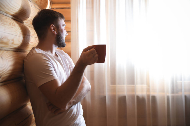 Man with drink near window indoors. Lazy morning - Zdjęcie, obraz