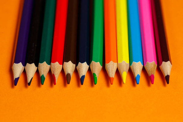 multicolored pencils for drawing stacked on an orange background. Stationery items - Photo, Image