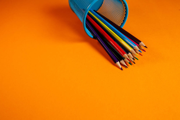 голубое металлическое ведро с цветными карандашами для офиса на оранжевом фоне
 - Фото, изображение