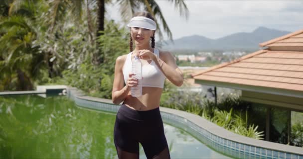 Schlanke Sportlerin trinkt Wasser in Schwimmbadnähe - Filmmaterial, Video