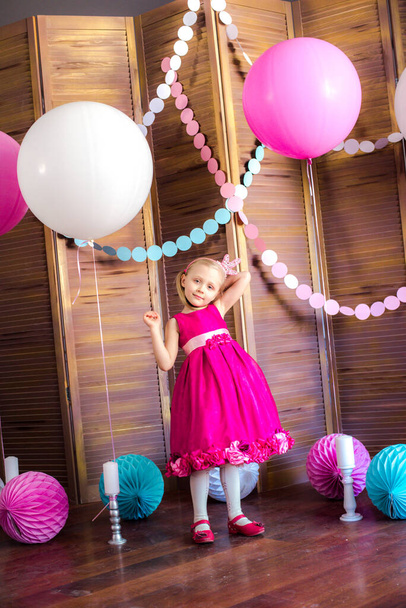 Little cute girl with blond hair in a pink dress and a princess crown with large bright balloons and garlands. Children's holiday. Children's decor. Balloons - Zdjęcie, obraz